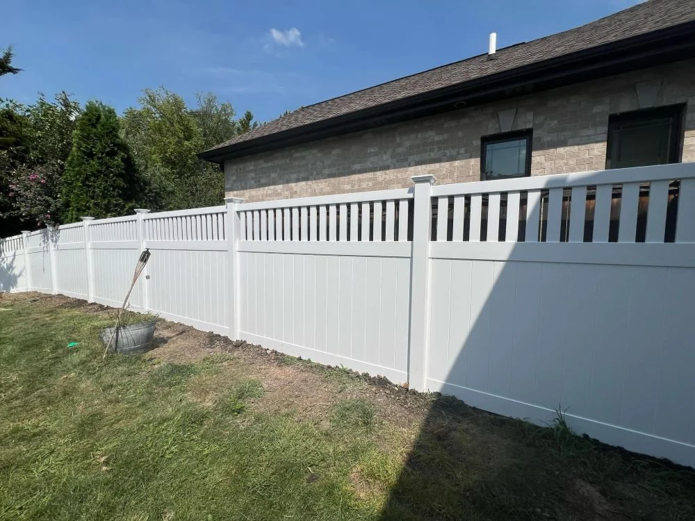 Elegant white vinyl privacy fence with solid lower panels and vertical picket accent on top beside brick home