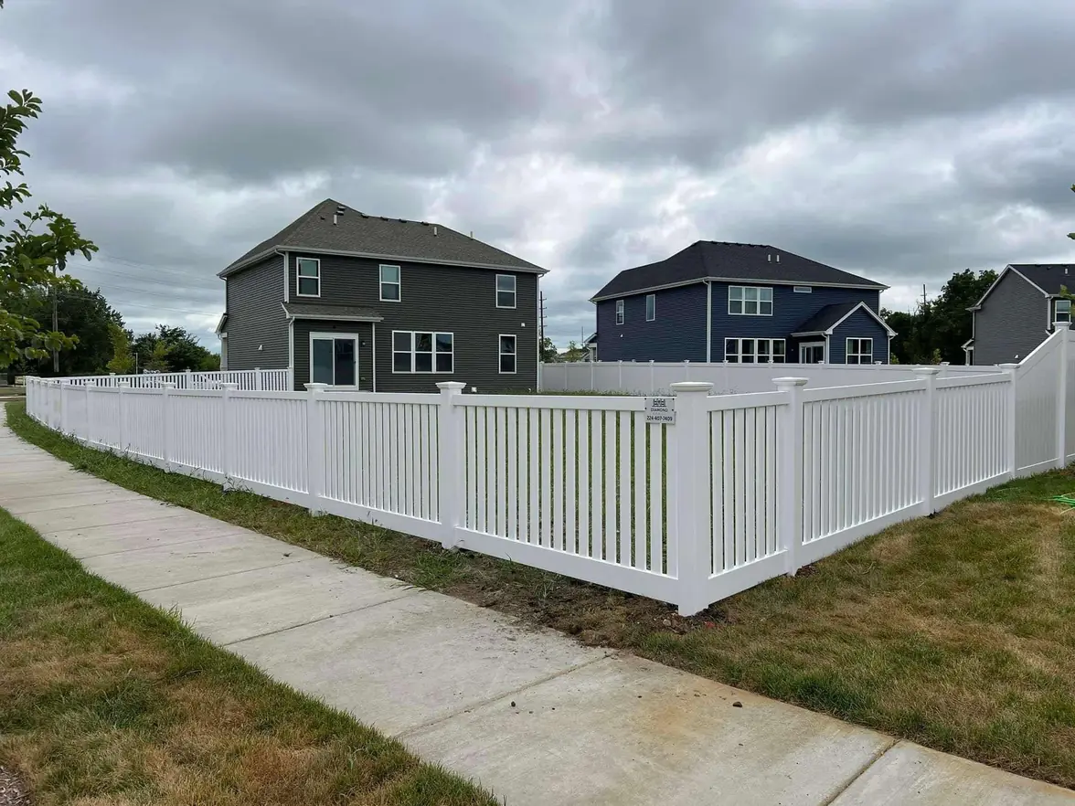 Modern white vinyl picket-style fence wrapping around new suburban homes, combining elegance and durability, with Diamond Fence sign along sidewalk