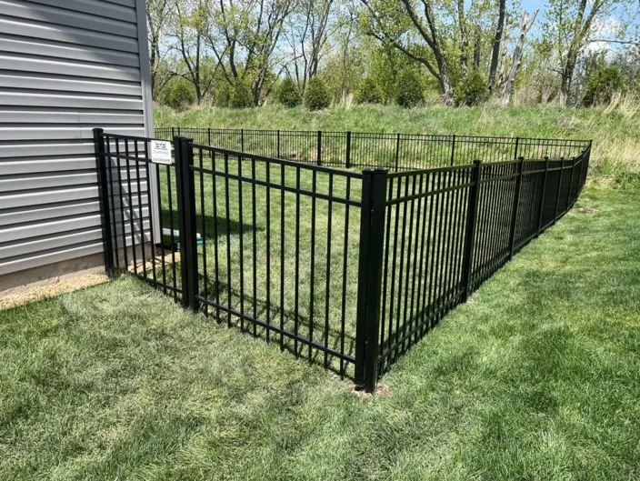 Newly installed black aluminum safety fence enclosing above-ground pool area on lush green lawn with gate access