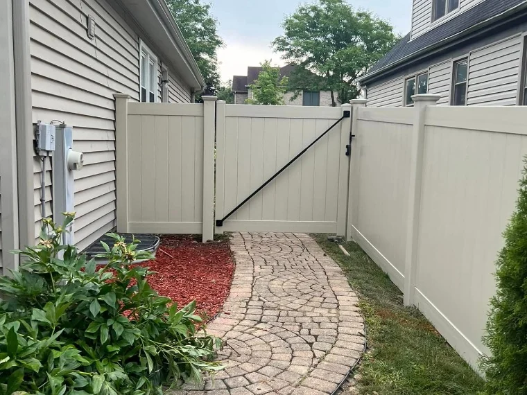 Elegant beige vinyl privacy fence framing curved paver pathway between homes with black diagonal brace gate